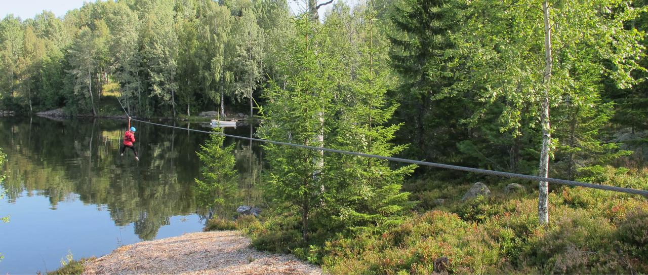 En som henger i en sele, svevende under en wire, høyt over Hurdalsjøen