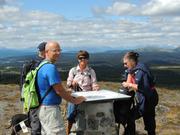 Bildet viser fire personer rundt sikteplata på toppen av Smørlifjellet. I bakgrunnen ses høyfjellene.