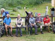 Trykk for å vise stort bildeFolk sitter på en benk med hver sin øl, kvinne står i bakgrunnen med hendene i været