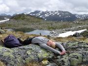 Trykk for å vise stort bildeKvinne ligger strak ut på en stein, vann og fjell i bakgrunnen