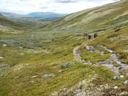 Ser utover en lang dal med vidt utsyn hvor en ser turdeltagere på vei på smale stier