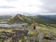 Bildet viser to mennesker på vei opp stien, setteovenifra. Terrenget er åpent og en ser fjellene i bakgrunnen.