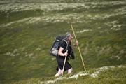 Bildet viser turlederen med en stokk og en ledsagerpinne på vei opp stien med en grønn skrent i bakgrunnen.