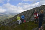 Bildet viser fire personer, hvor to sitter og blir tatt bilde av med en flott utsikt mot fjell i bakgrunnen.