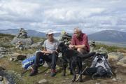 To personer i gruppen hviler sittende på en sten mens en hund ser på maten de har i hendene.